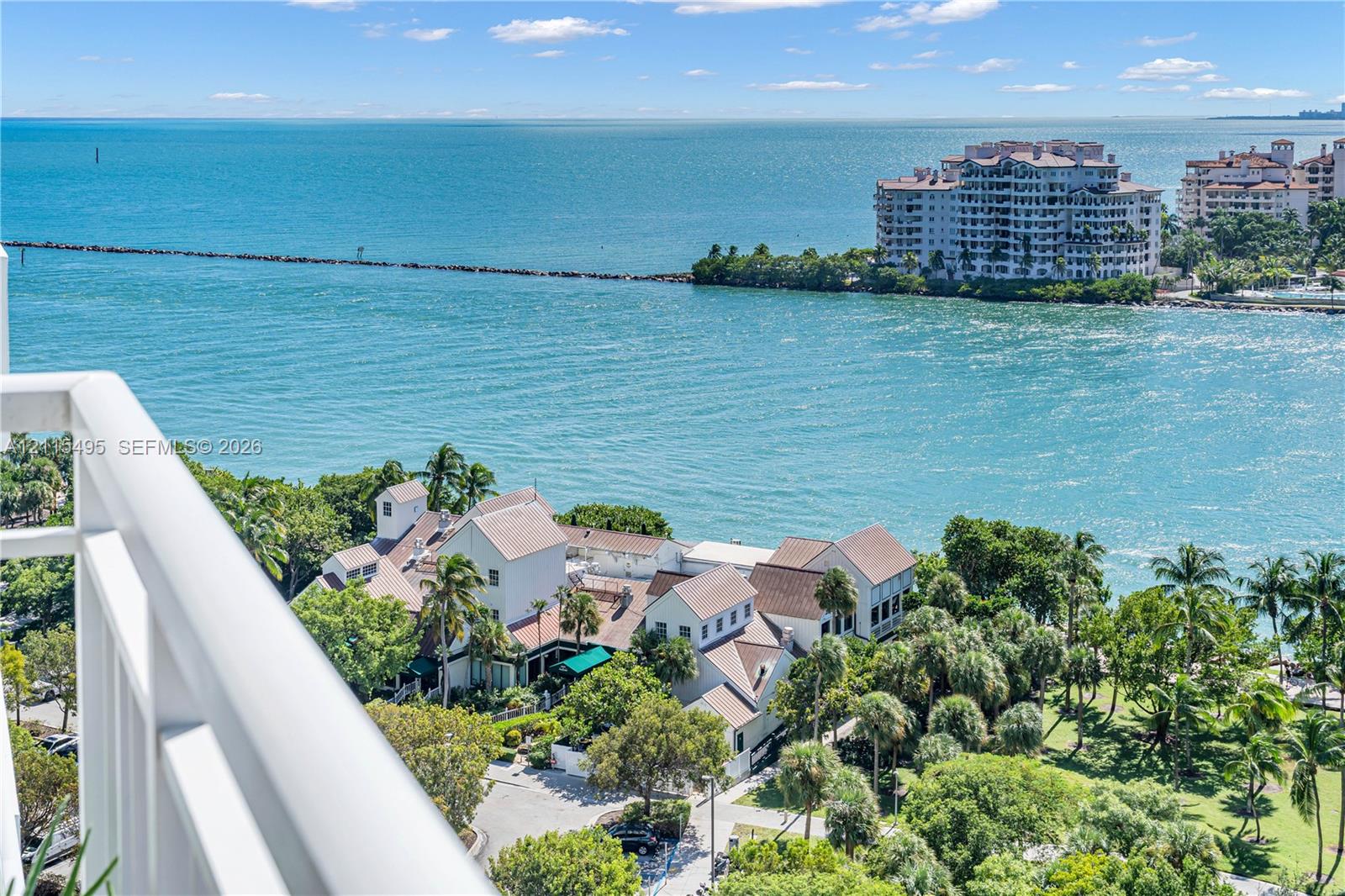 Elevated balcony featuring a white metal railing and expansive coastal water scenery with tropical landscaping and mature palm trees