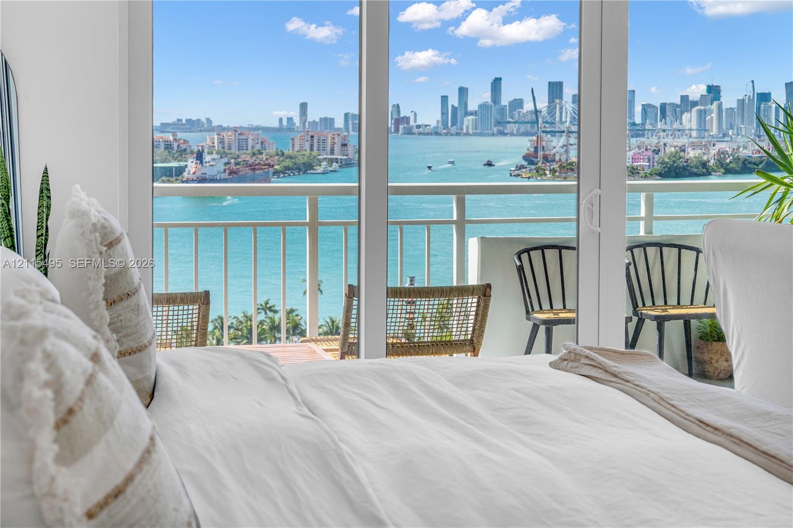 Floor-to-ceiling sliding glass doors opening to a private balcony with railing, featuring a coastal and urban skyline backdrop