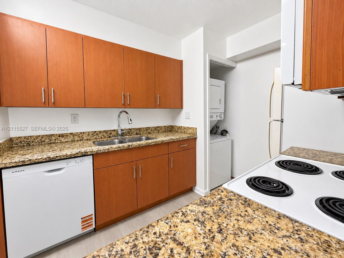 Kitchen featuring wood-finish cabinetry, stone-finish countertops, stainless steel dual-basin undermount sink with arched faucet, built-in dishwasher, and recessed laundry alcove