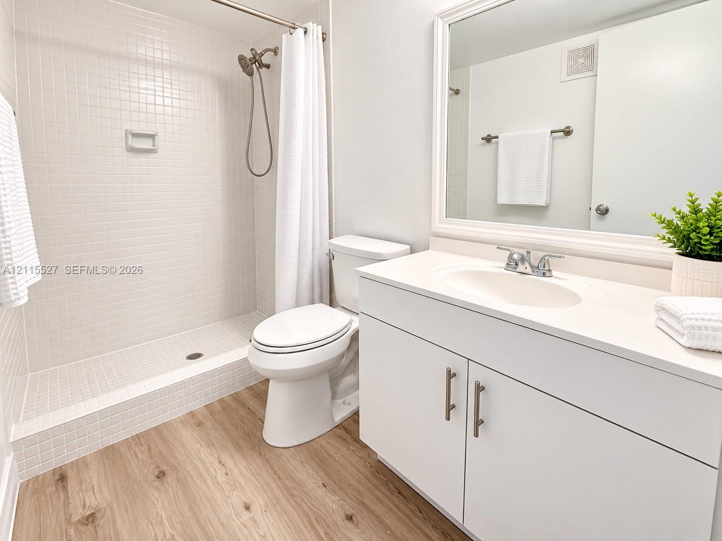 Bathroom featuring a white vanity with an integrated basin, wood-finish flooring, and a walk-in shower with white tile surround