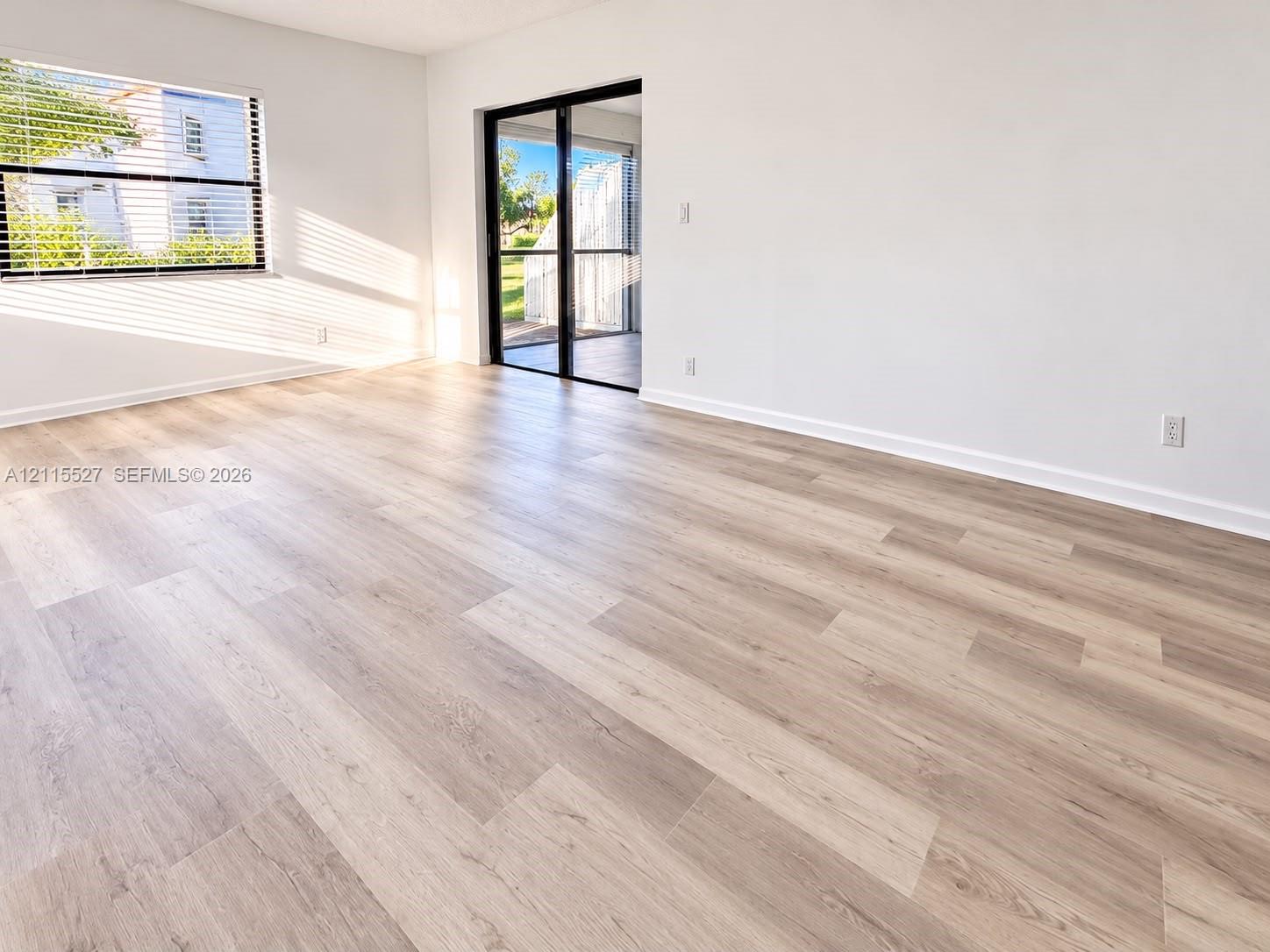 Interior space featuring light-toned wood-finish flooring, white walls, horizontal window blinds, and black-framed sliding glass doors