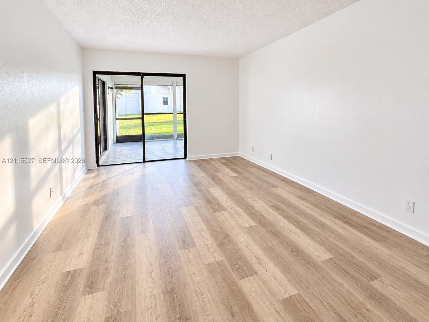 Interior space featuring neutral wall paint, wood-finish flooring, and a sliding glass door with black trim opening to a screened patio