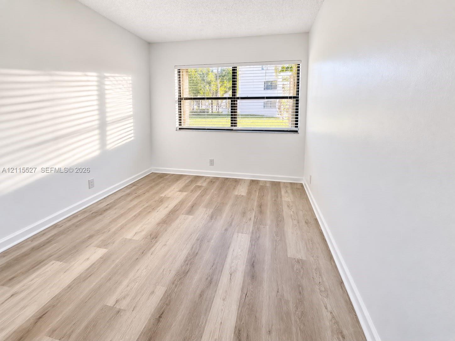 Neutral interior space featuring wood-finish flooring, a large window, and minimalist white walls