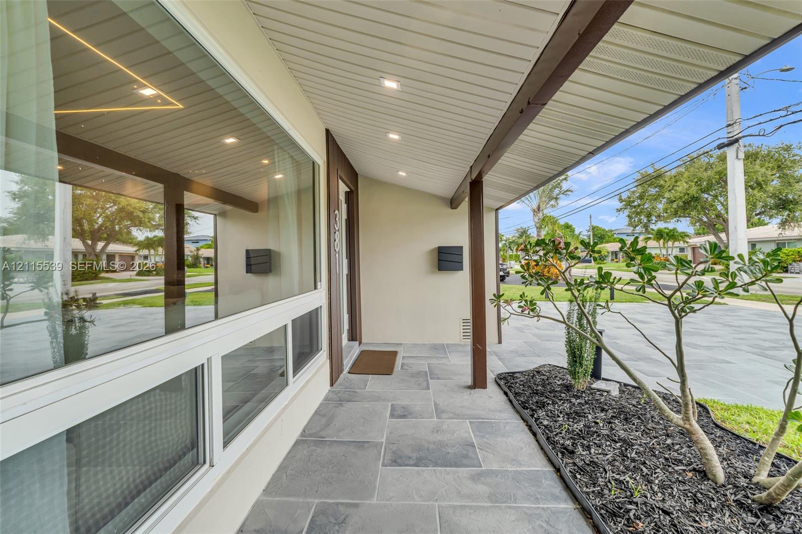 Covered entryway featuring large-format grey stone floor tiles, recessed ceiling lighting, a sprawling paneled window, and dark wood-finish structural support beams