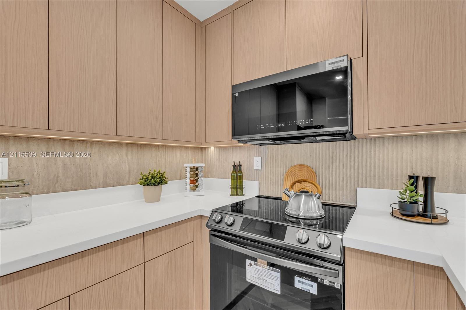 Flat-panel light wood cabinetry featuring under-cabinet lighting, solid surface countertops, textured backsplash, and herringbone-pattern wood-finish flooring