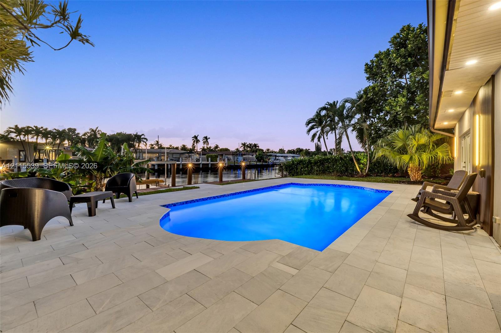 In-ground pool featuring a stone-paver deck, waterfront bulkhead, and integrated recessed lighting