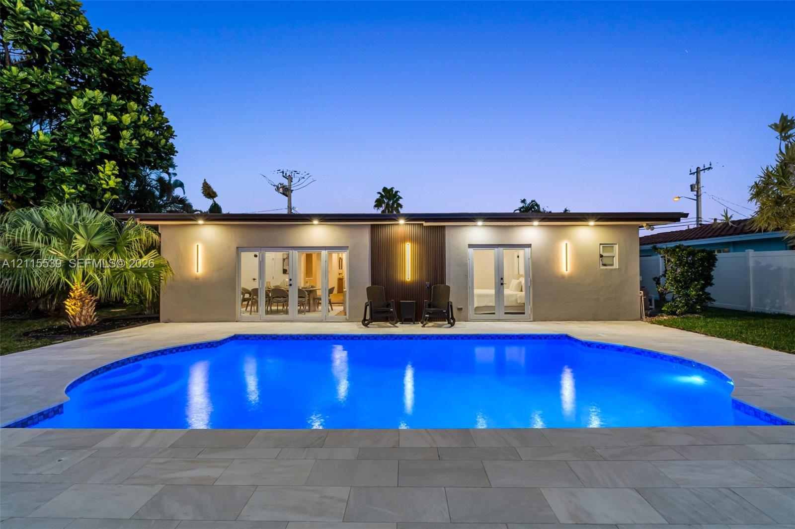 Swimming pool with stone-tile decking, dual sets of French doors, recessed ceiling lighting, and vertical exterior wall-mounted fixtures
