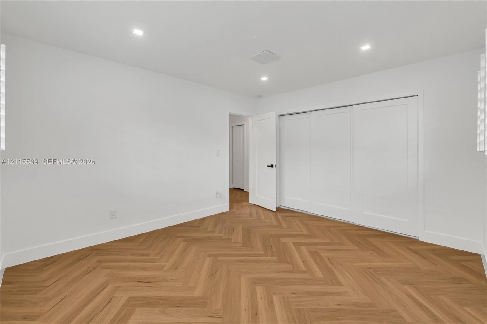 Herringbone wood-finish flooring, recessed lighting, and three-panel sliding closet doors with matte black hardware