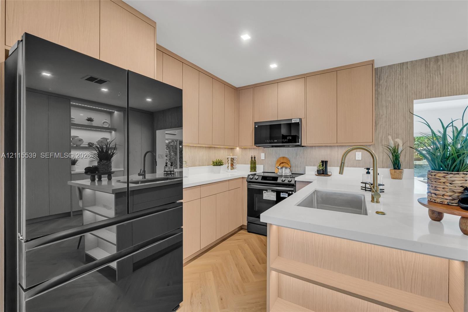 Kitchen featuring flat-panel wood cabinetry, light-toned stone countertops, herringbone-patterned wood flooring, integrated under-cabinet lighting, and a stainless steel undermount sink with a high-arch brass faucet