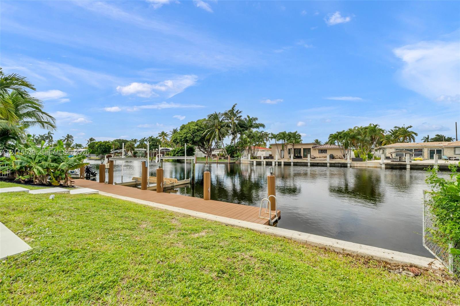 Waterfront property featuring a synthetic wood-plank dock, concrete seawall, and private boat lift