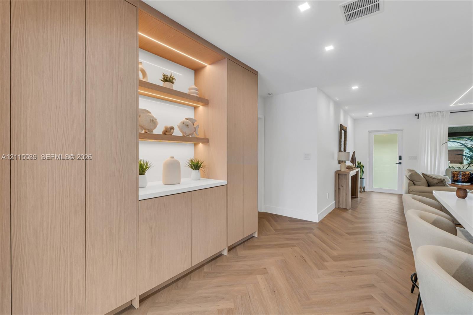 Custom floor-to-ceiling cabinetry featuring integrated LED display shelving, smooth-surface countertops, and light-tone wood finish flooring in a herringbone pattern