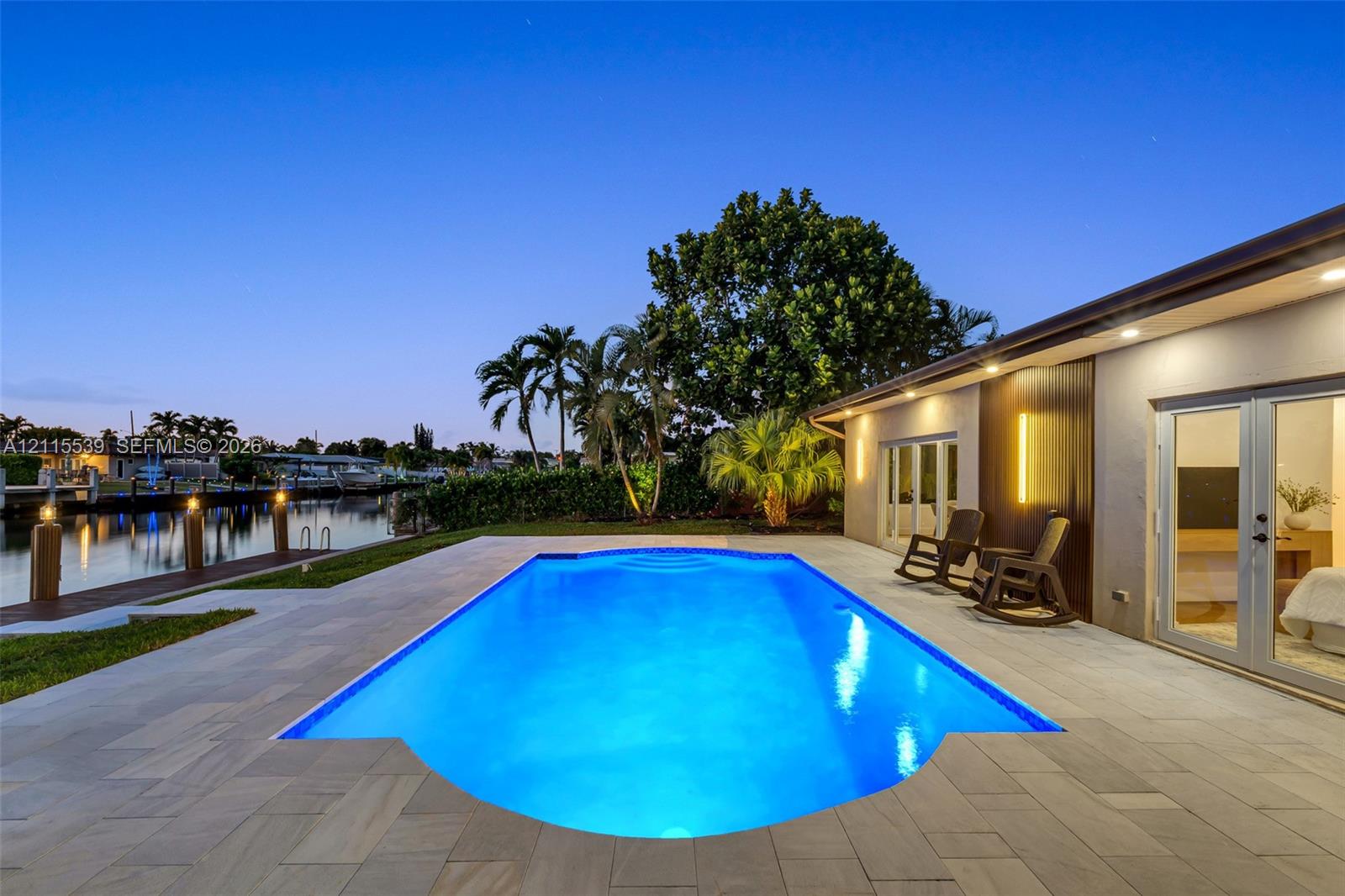 In-ground swimming pool with stone-tiled patio, waterfront bulkhead, and private boat dock