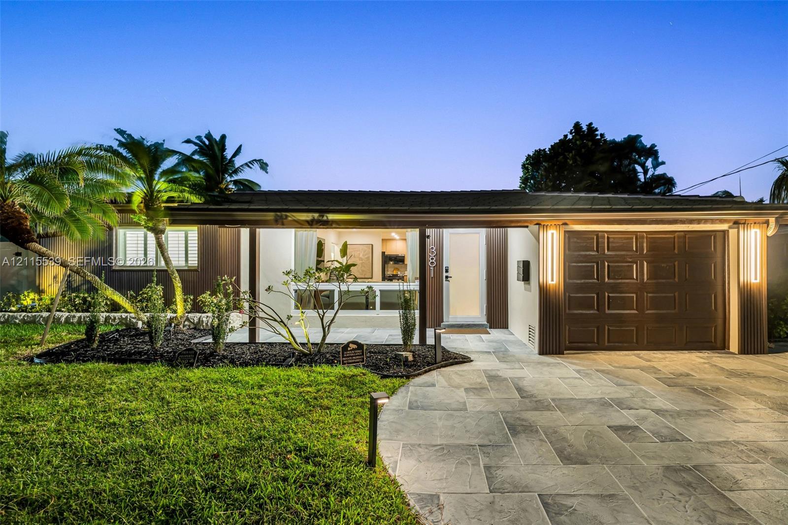 Single-story exterior featuring a natural stone-patterned paved driveway, integrated vertical exterior wall lighting, and landscaped front lawn with mature palm trees
