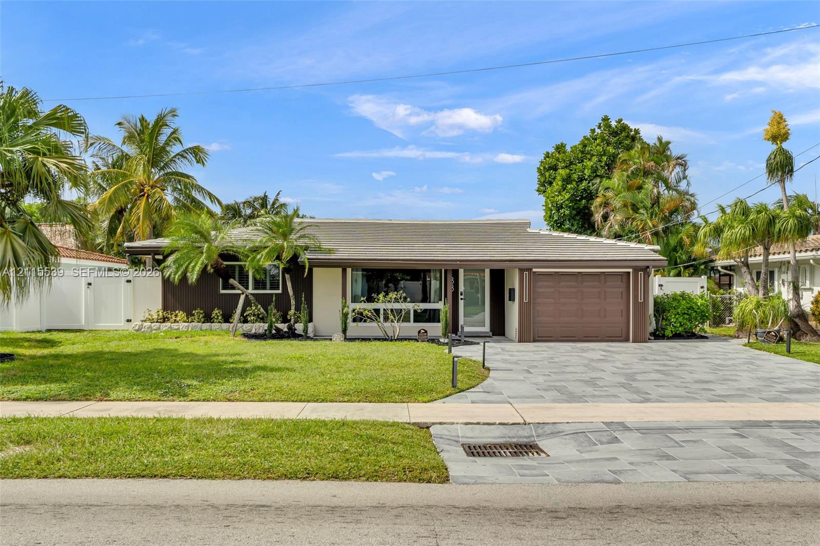 Single-story residence featuring a multi-toned exterior, a natural stone paved driveway, an attached garage, and mature palm landscaping