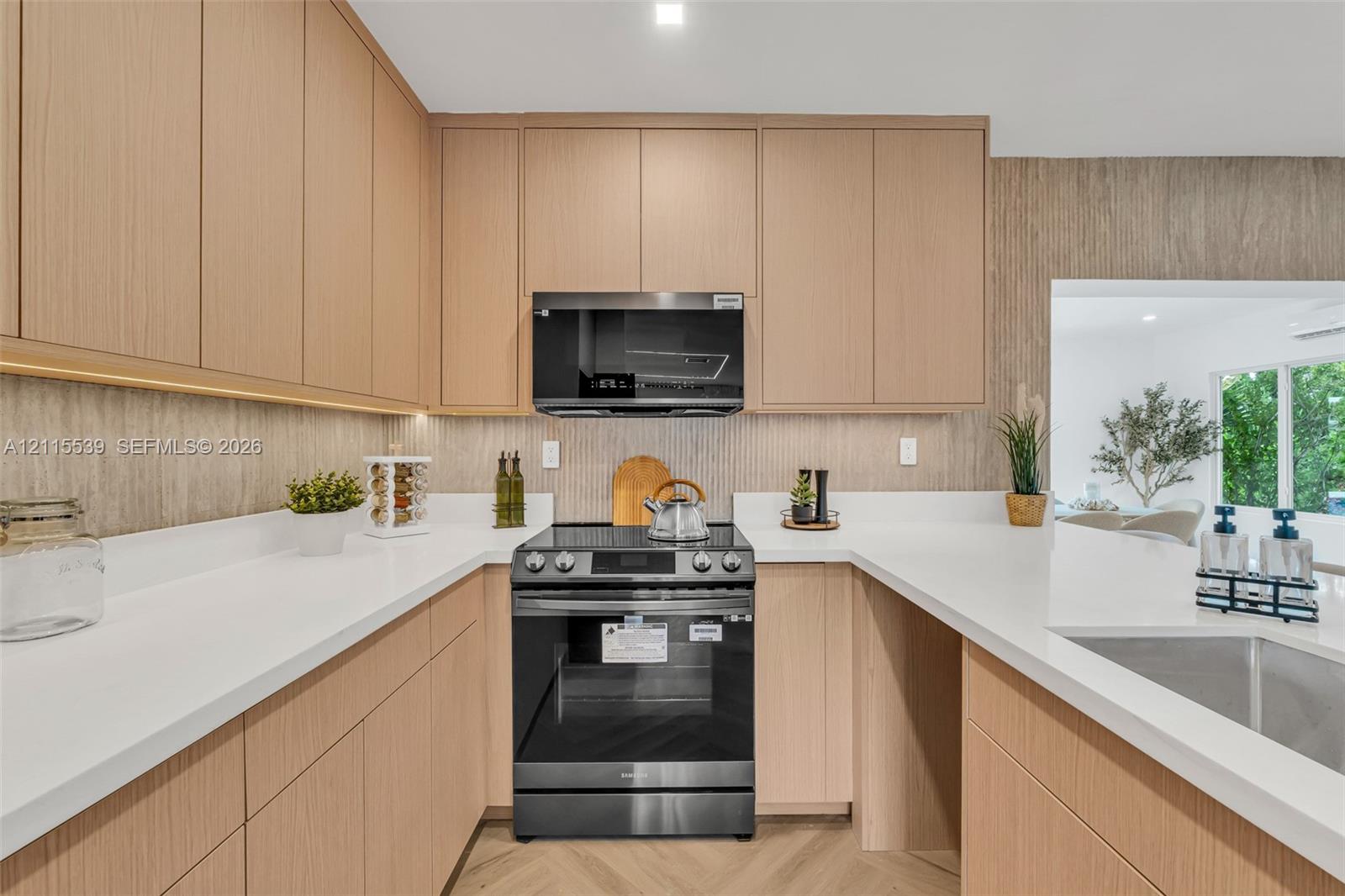 Kitchen featuring light wood-finish cabinetry, quartz countertops, vertical textured backsplash, stainless steel microwave, and chevron-patterned flooring