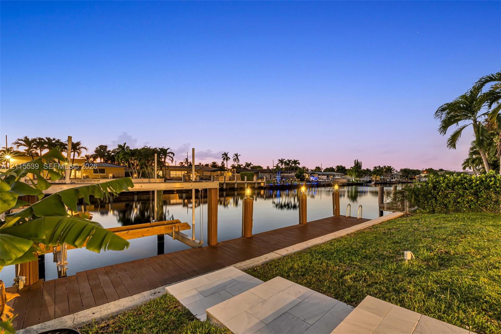 Waterfront property featuring a private dock, boat lift, manicured lawn, and stone paver walkway