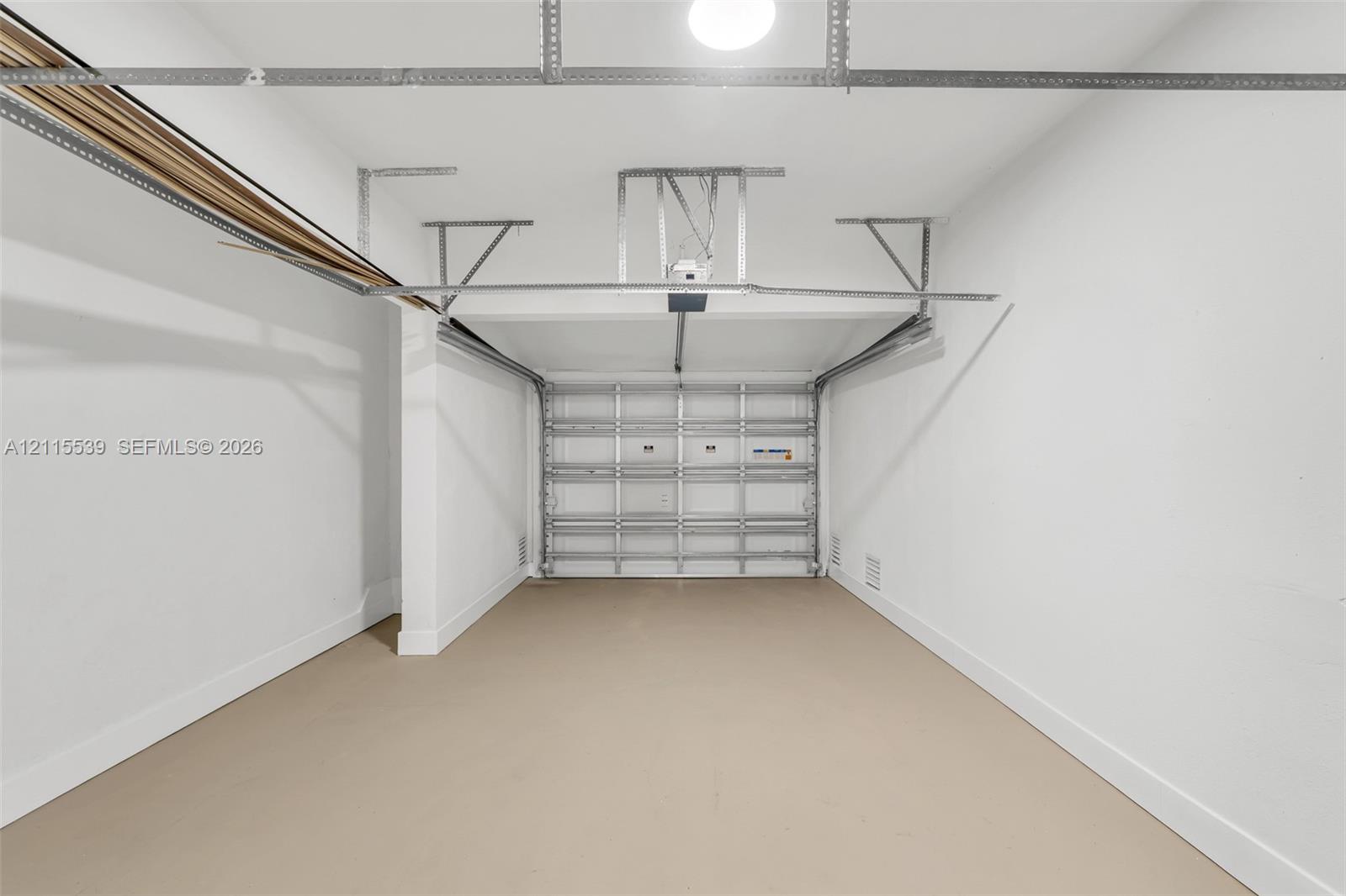 Enclosed garage featuring finished concrete flooring, painted walls, an automated sectional door, and overhead lighting