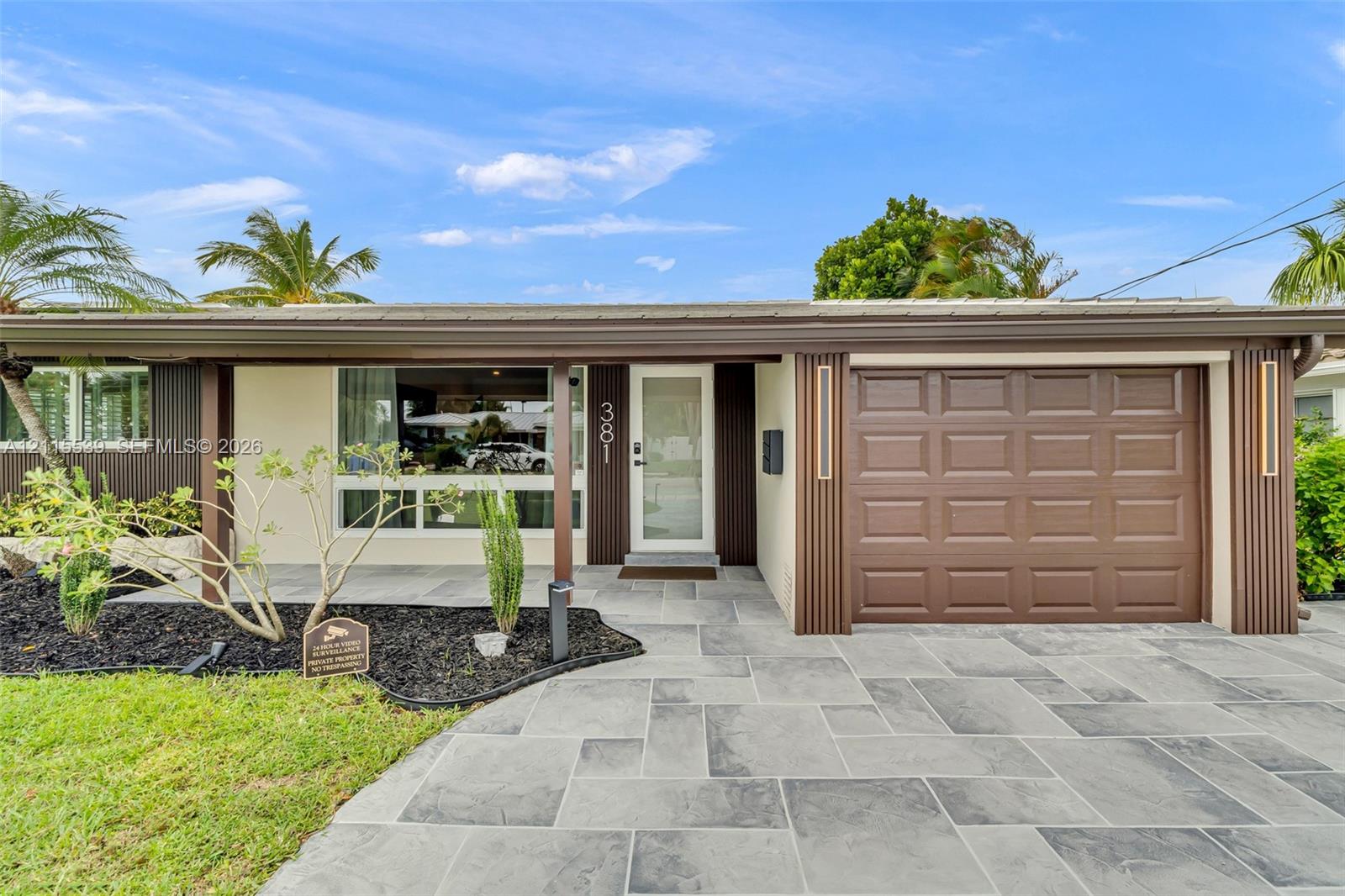 Single-story exterior featuring a stone-paver driveway, integrated garage with a paneled door, covered front entryway, and vertical wood-slat accent siding