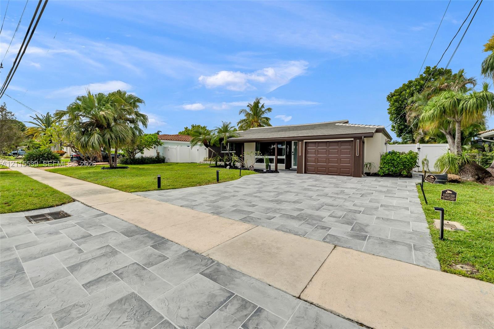 Single-story residence featuring a stone-paver driveway, attached garage with a multi-panel door, and white vinyl perimeter fencing