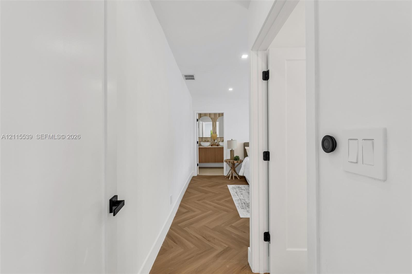 Hallway featuring wood-finish flooring in a herringbone pattern, matte black door hardware, and crisp white walls