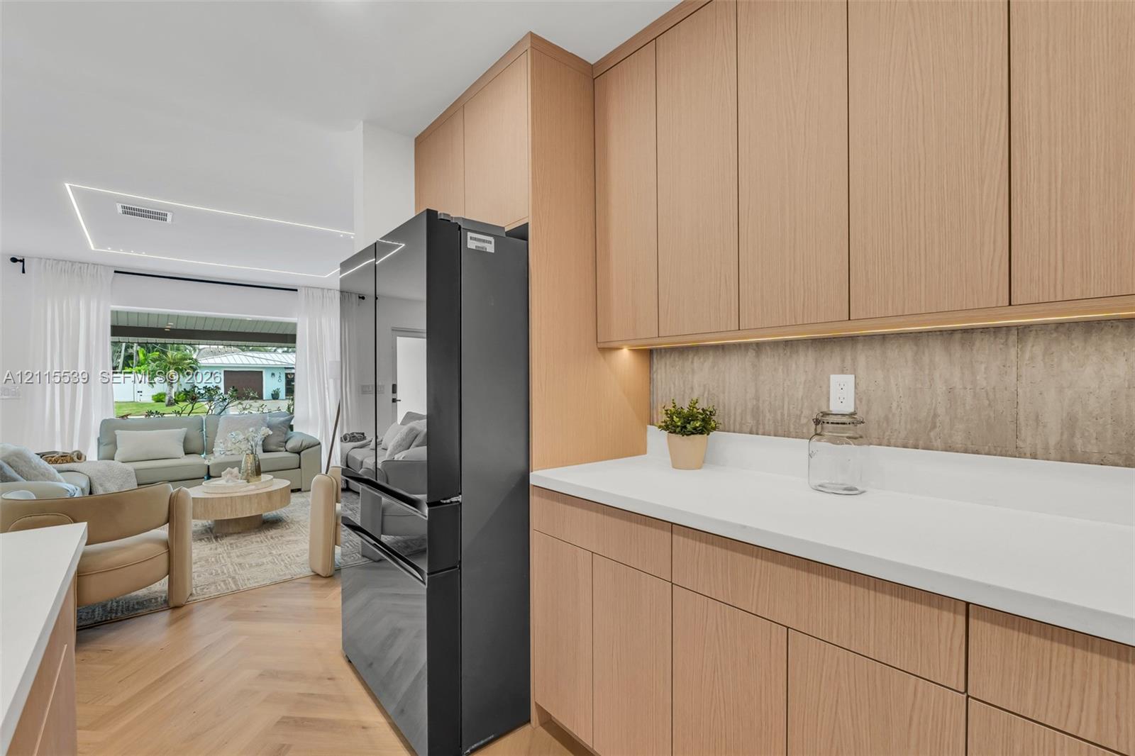 Flat-panel light wood cabinetry featuring under-cabinet lighting, solid surface countertops, textured backsplash, and herringbone-pattern wood-finish flooring