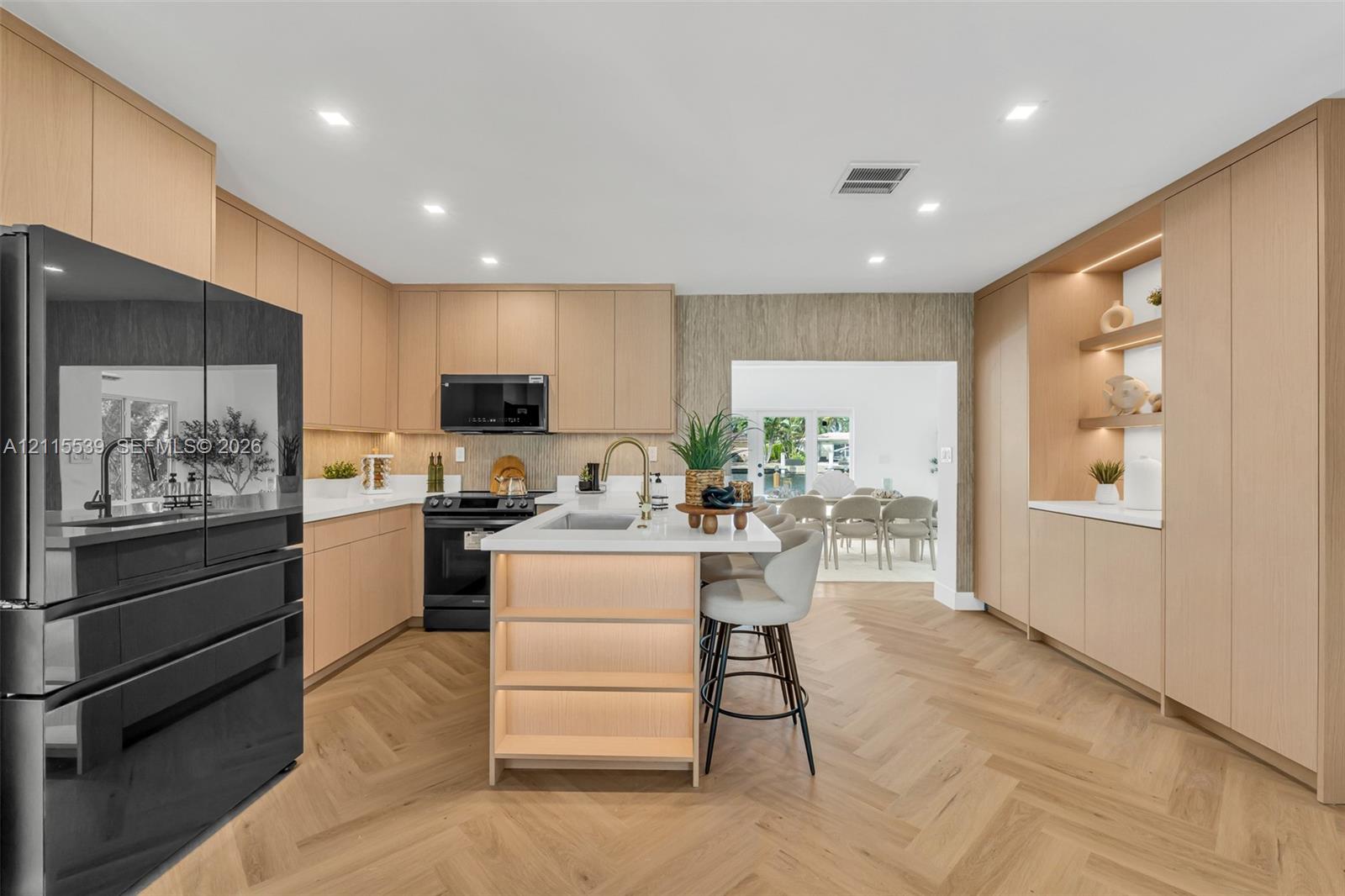 Kitchen featuring light wood-finish cabinetry, herringbone-patterned wood flooring, a central island with an integrated sink and under-counter lighting, and built-in floor-to-ceiling storage