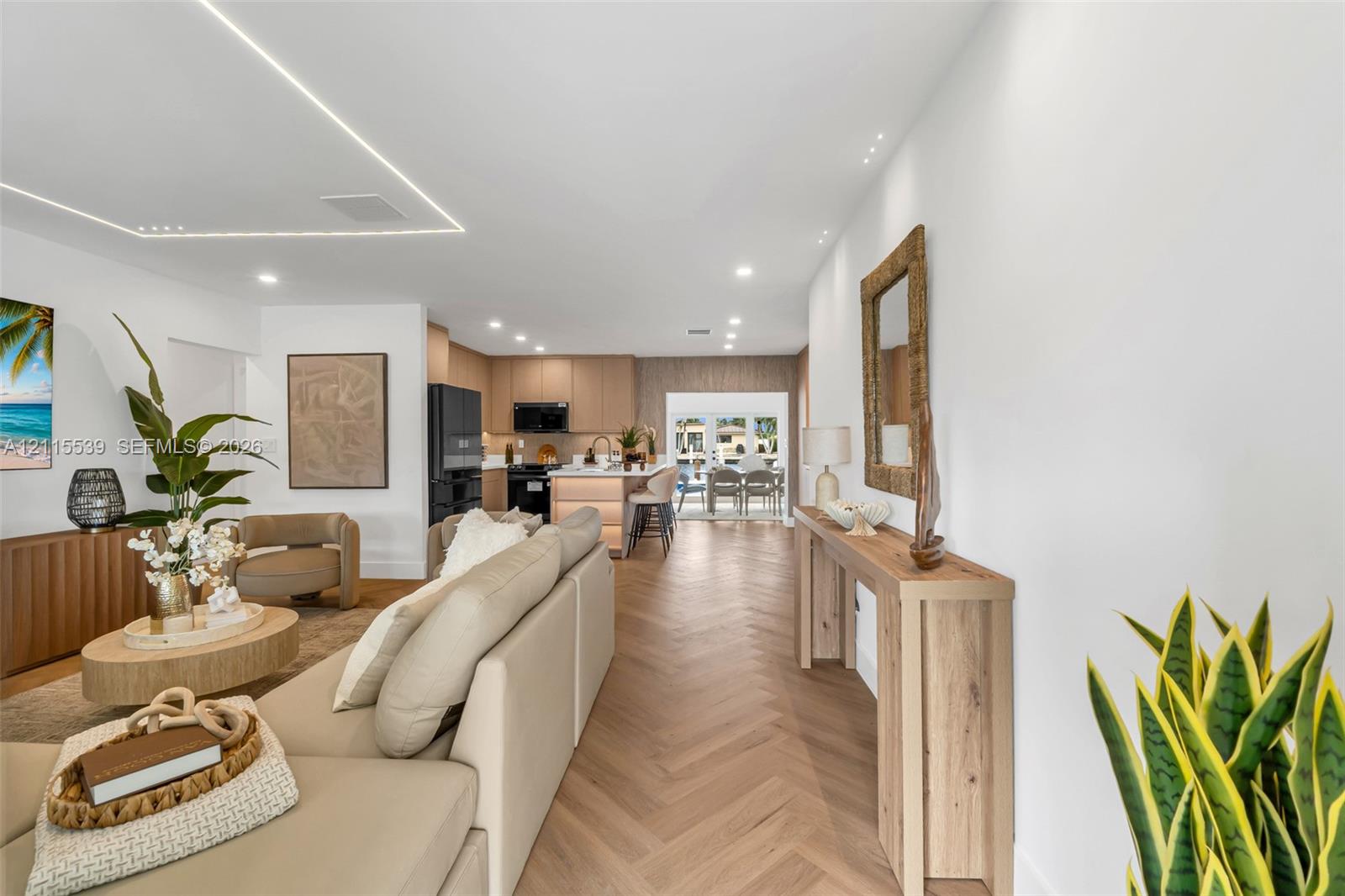 Herringbone wood-finish flooring, recessed ceiling lighting, linear architectural cove lighting, kitchen island with built-in cabinetry, and integrated black appliances