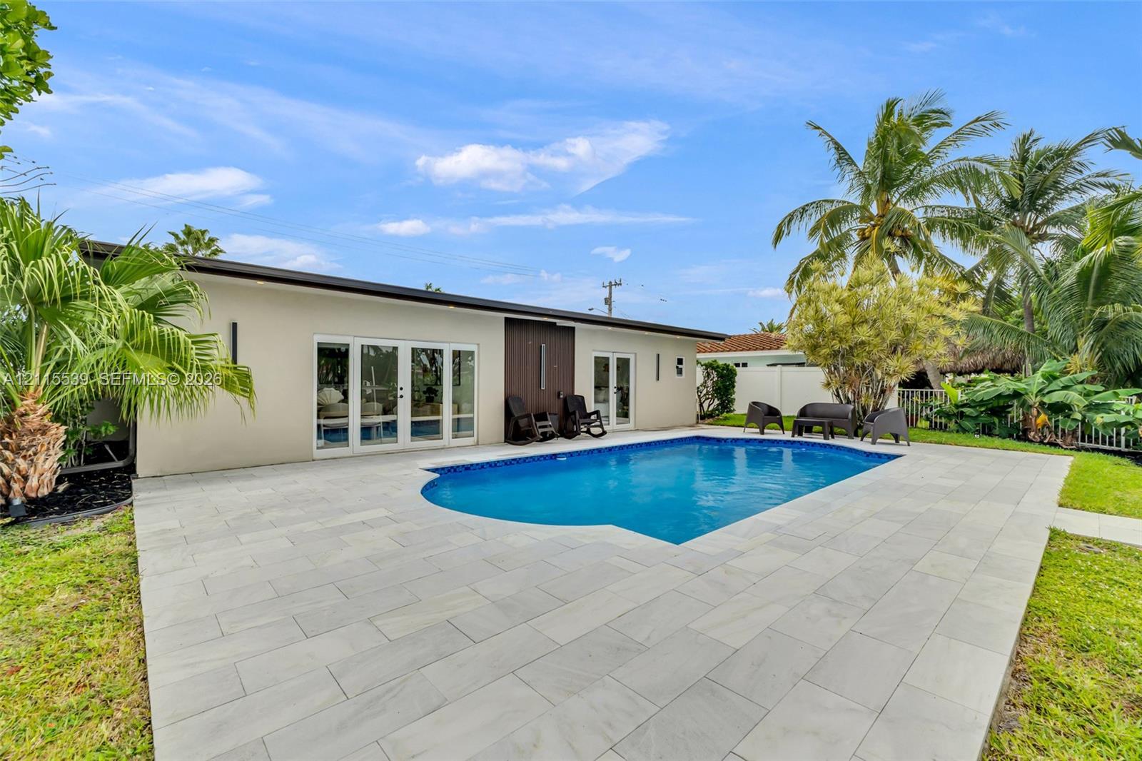 Rear exterior featuring an in-ground swimming pool, expansive stone paver patio, multi-panel glass door systems, and mature landscaping