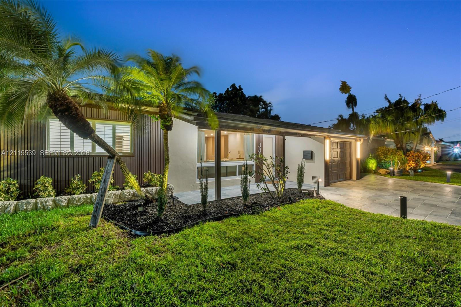 Single-story exterior featuring corrugated metal siding, stucco finish, stone landscape edging, and a paved driveway