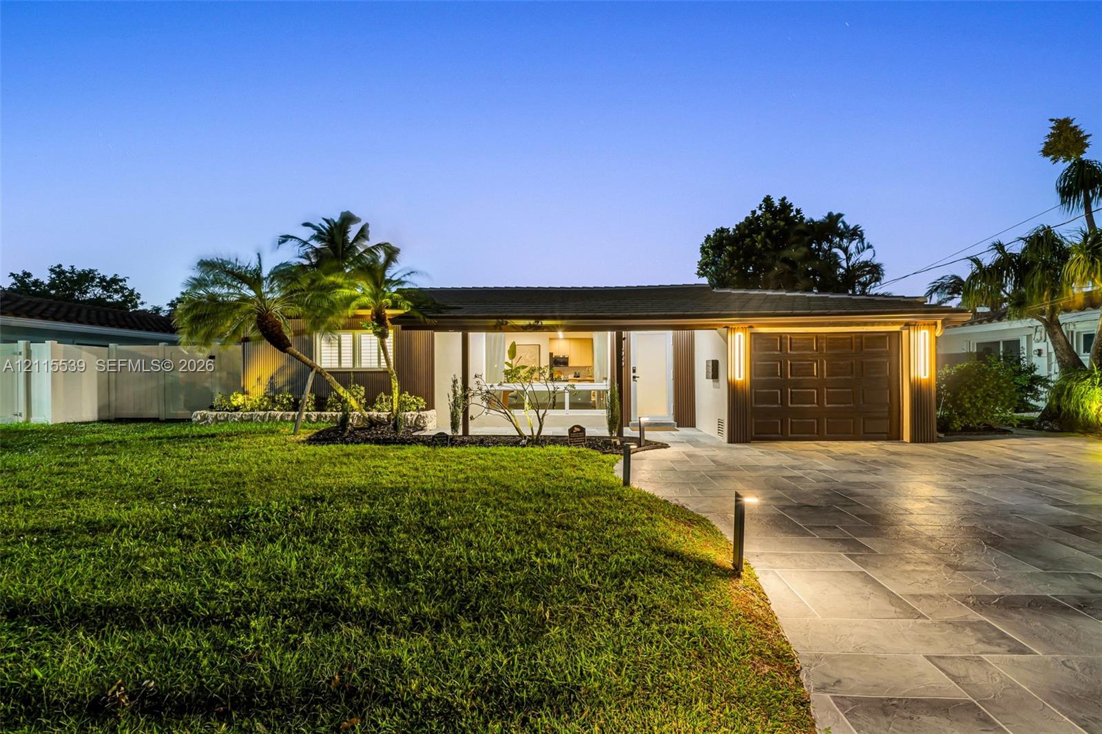 Single-story residence featuring a paved driveway, integrated garage with sectional door, low-pitched roof, manicured lawn, and professional exterior landscape lighting