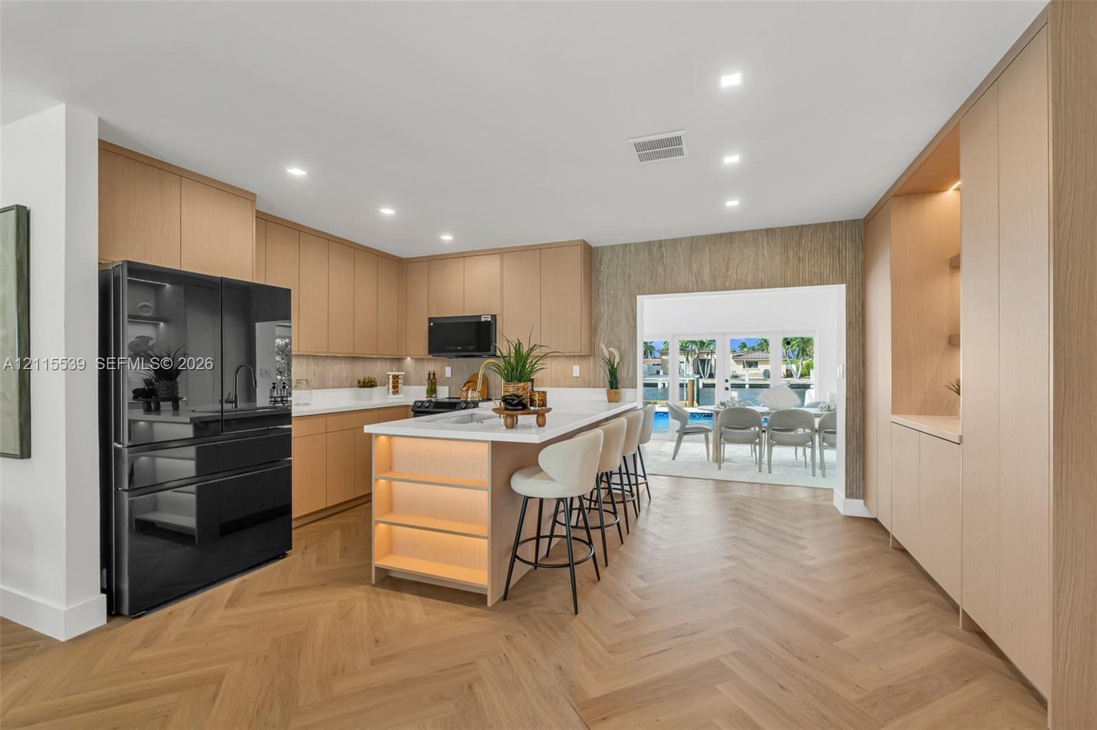 Kitchen featuring custom light wood cabinetry, white stone countertops, herringbone patterned wood-finish flooring, recessed lighting, and a center island with integrated under-counter illumination