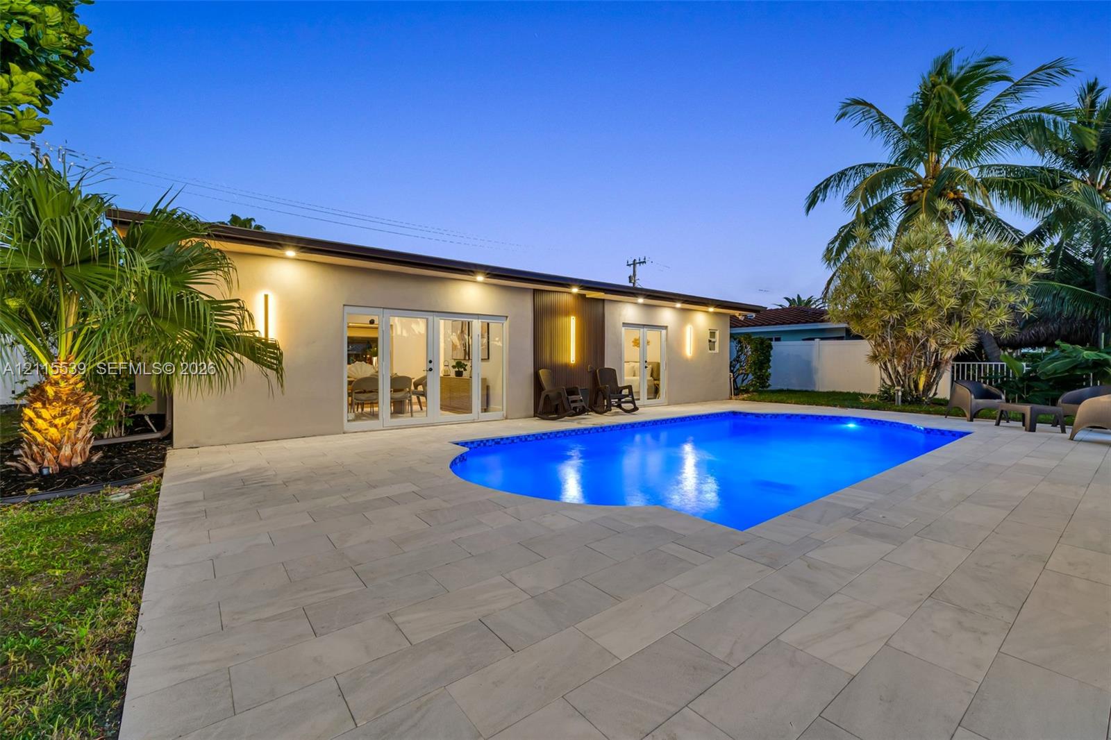 Outdoor space featuring a swimming pool, large-format paver patio, double French doors, and exterior wall-mounted accent lighting