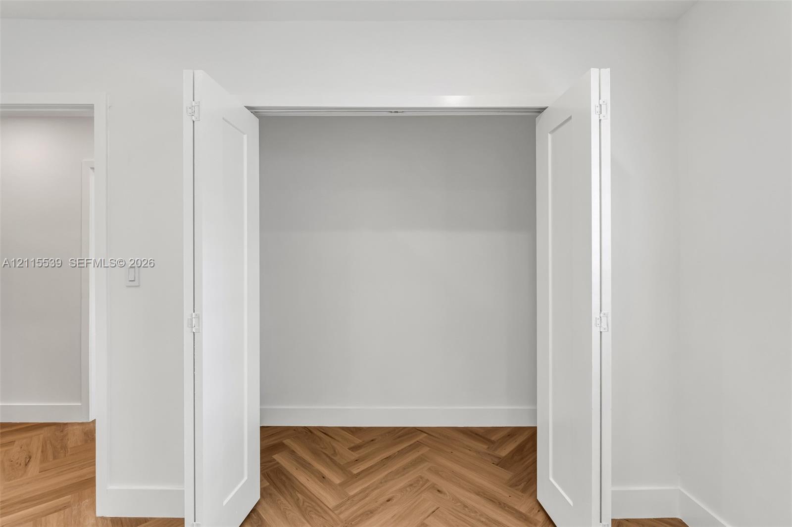 White bi-fold closet doors featuring a two-panel design and wood-finish herringbone flooring