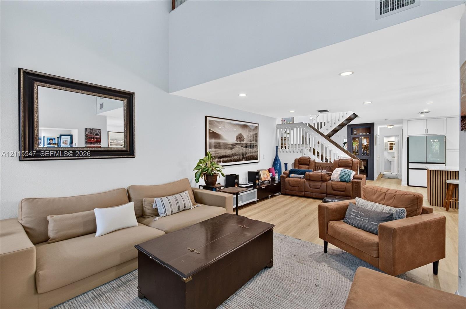 Double-height ceilings, wood-finish flooring, recessed lighting, and a staircase featuring a white balustrade with a wood handrail