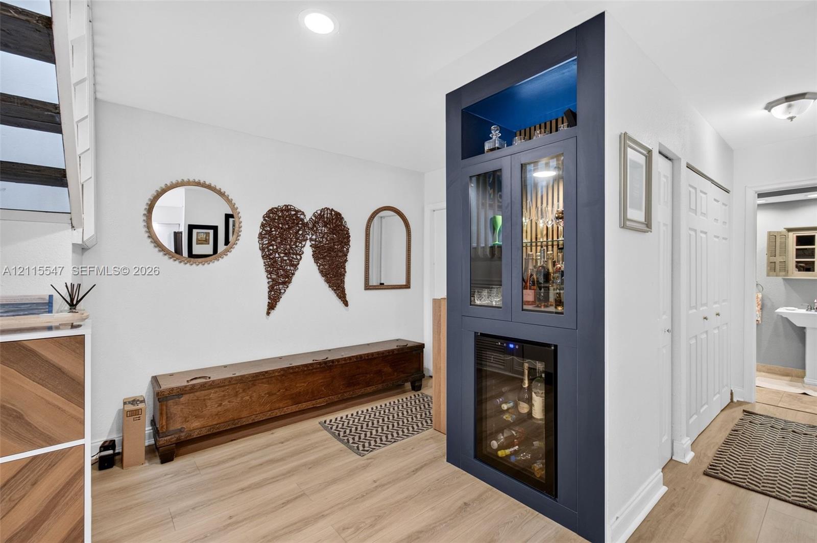 Built-in dark navy cabinetry featuring glass-front display shelving, recessed lighting, and an integrated beverage refrigerator, complemented by wood-finish flooring and recessed ceiling lighting