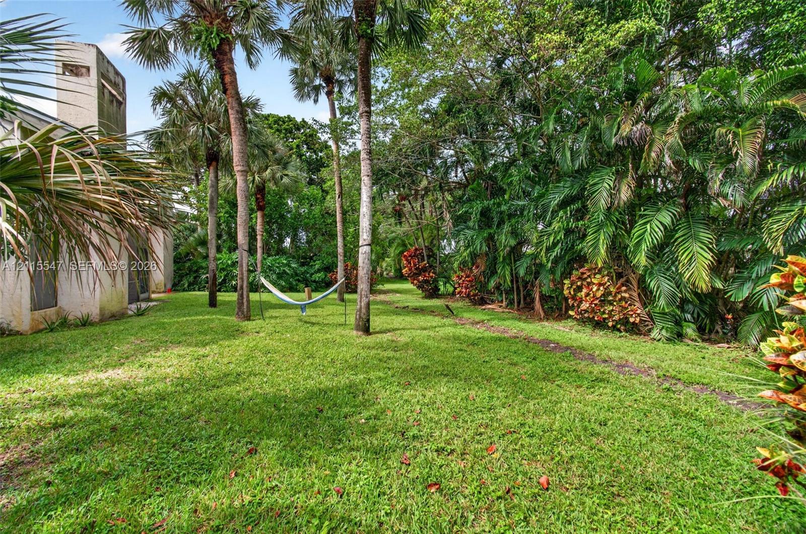 Expansive lawn area featuring mature palm trees, dense tropical foliage, and a textured stucco exterior chimney