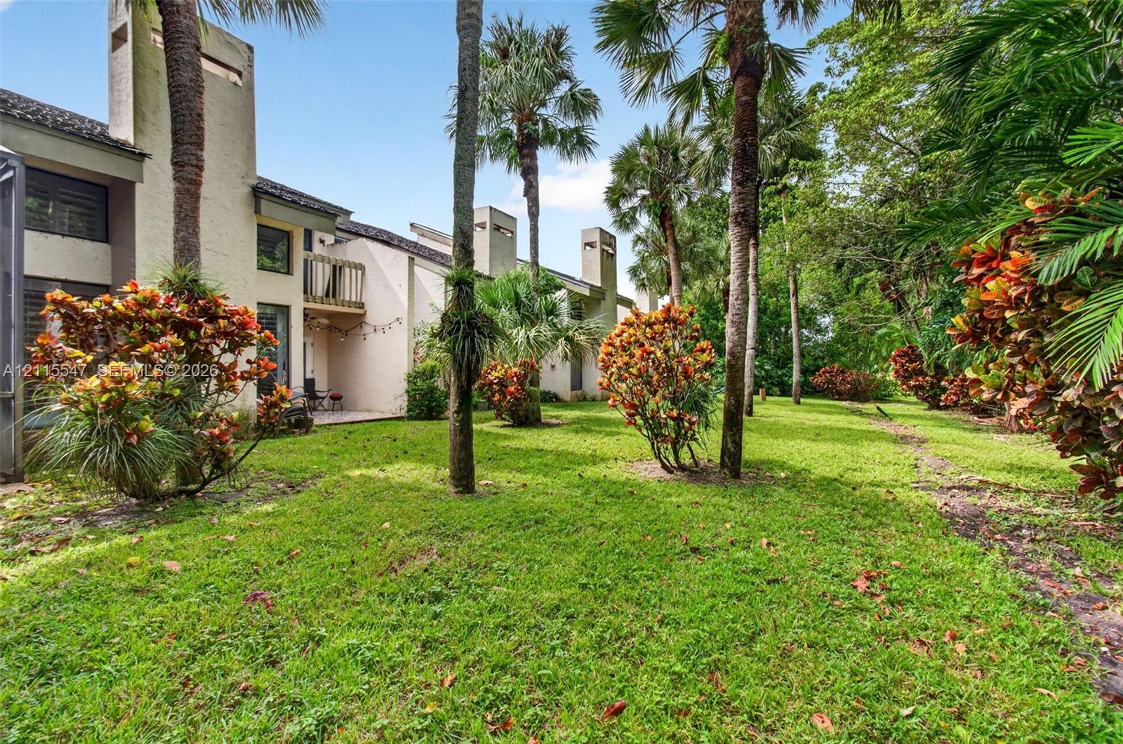 Stucco exterior featuring multiple chimney stacks, a second-story wooden balcony, and established palm trees within a landscaped grounds area