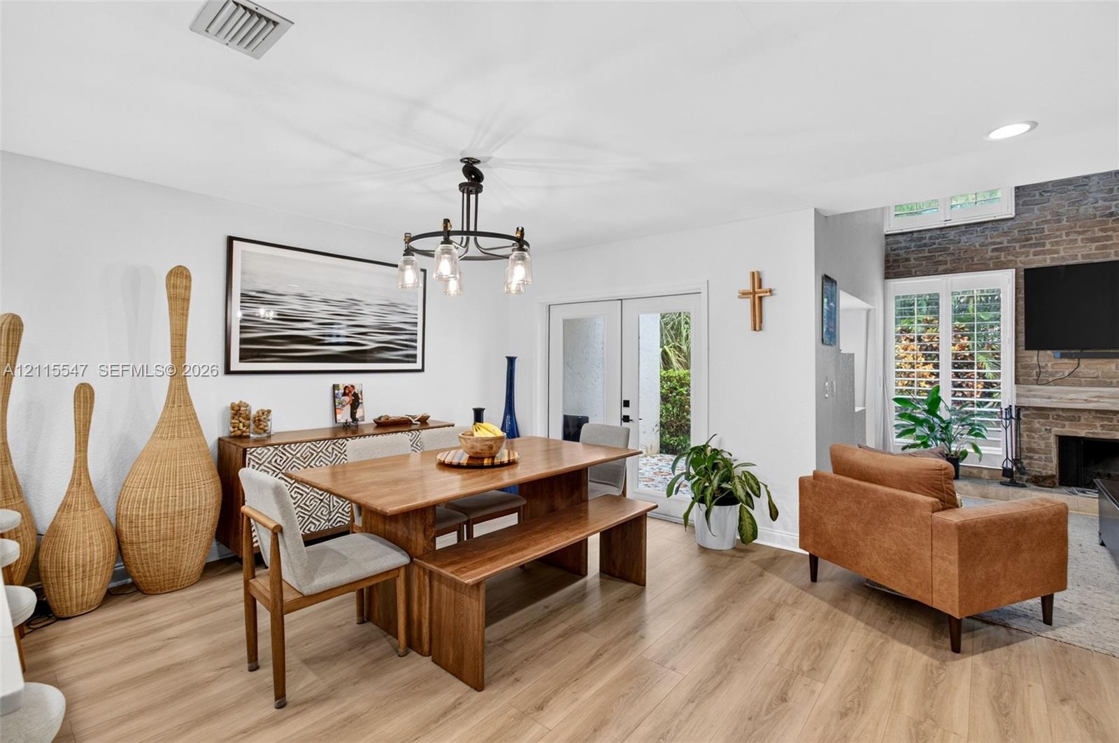 Open-concept room featuring wood-finish flooring, a multi-arm iron chandelier, double glass-paneled exterior doors, and a floor-to-ceiling decorative brick fireplace with a wood mantel