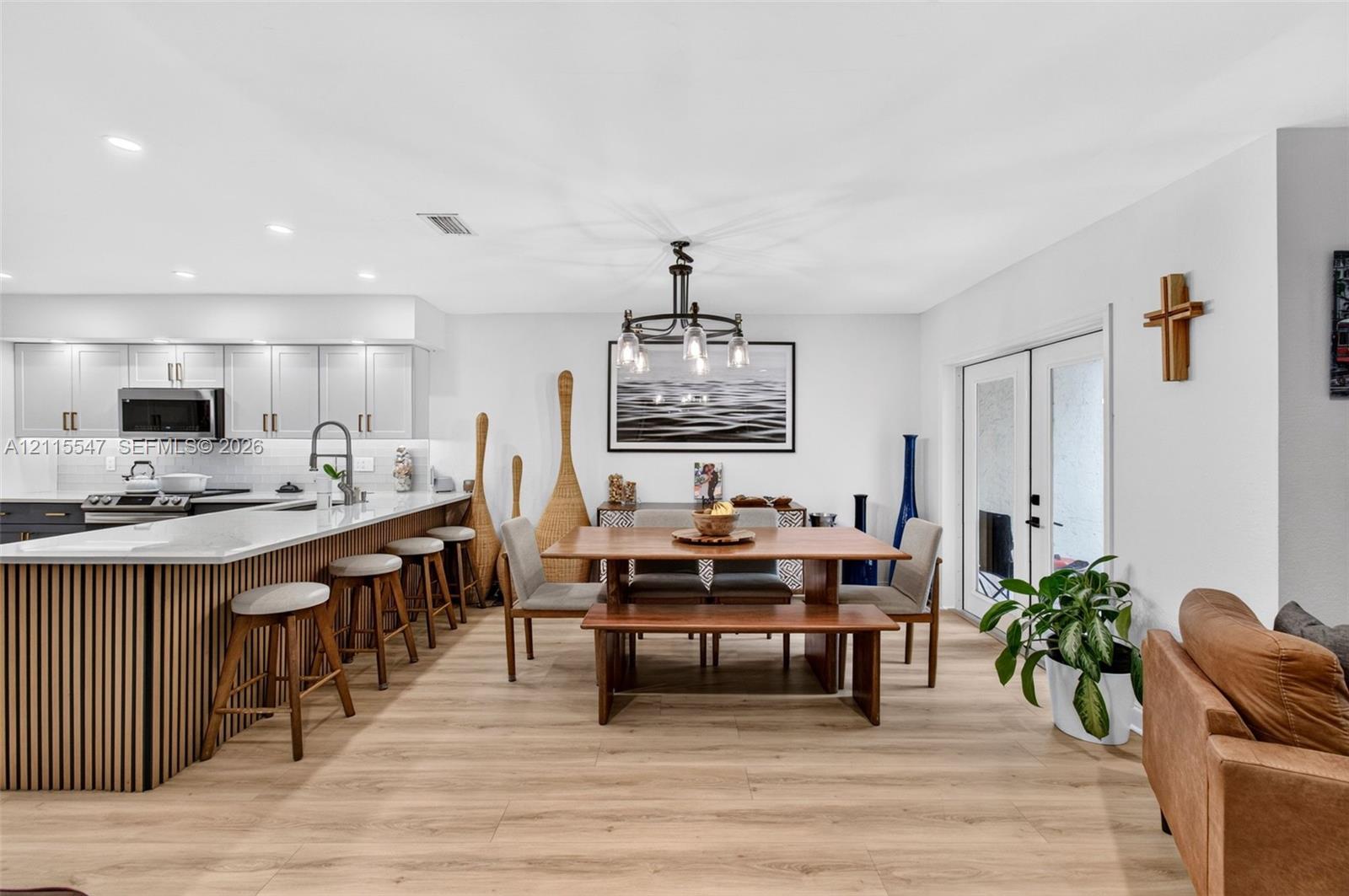 Open-concept kitchen and dining area featuring wood-finish flooring, a kitchen island with vertical wood-slat detailing, quartz countertops, recessed lighting, and double glass doors