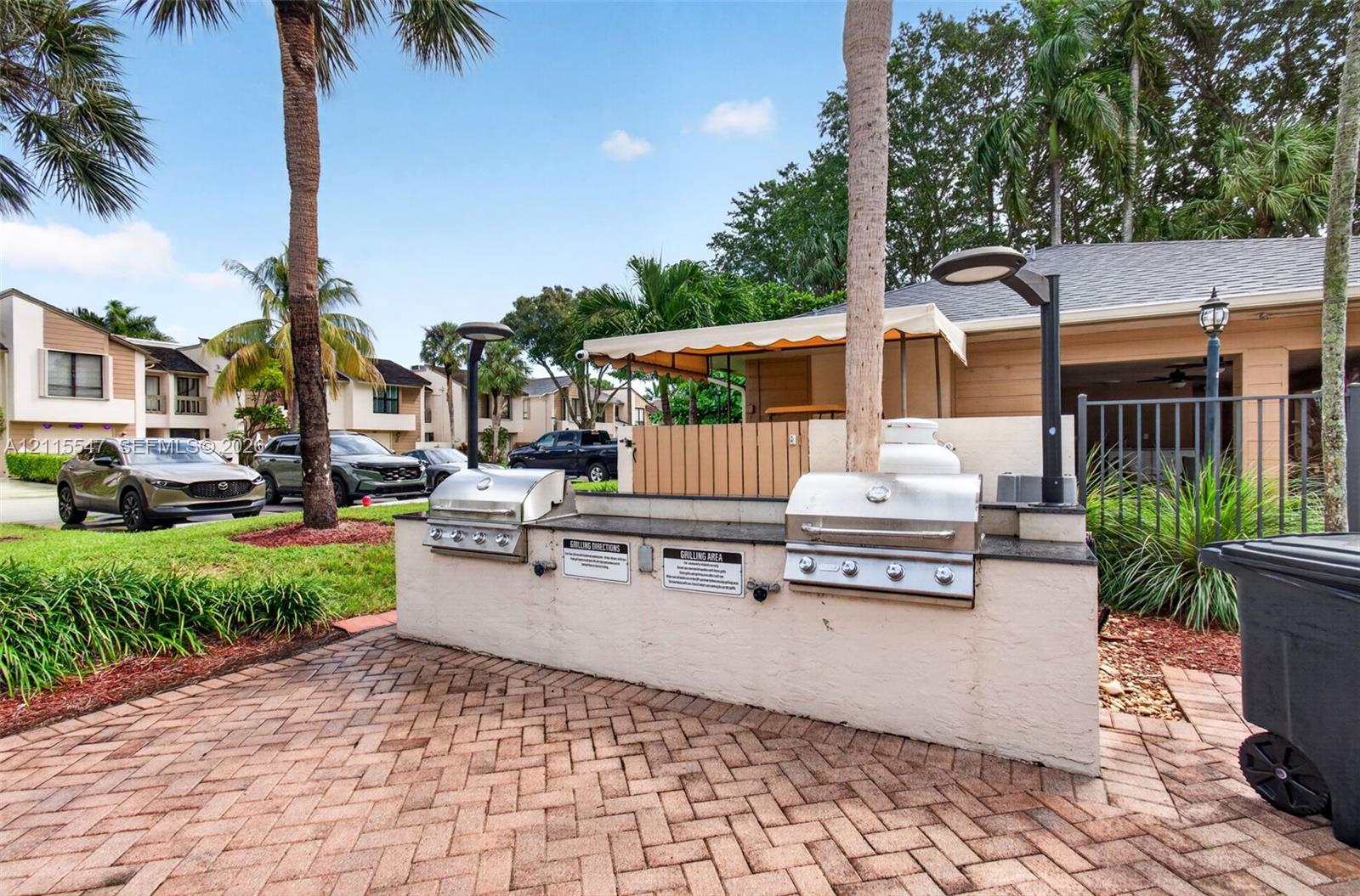 Outdoor grilling station featuring dual stainless steel built-in grills, stone countertop, brick-paver flooring, and integrated lighting