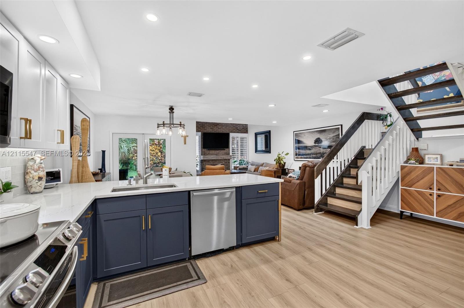 Kitchen featuring navy cabinetry, quartz countertops, stainless steel appliances, wood-finish flooring, and a staircase with a white balustrade