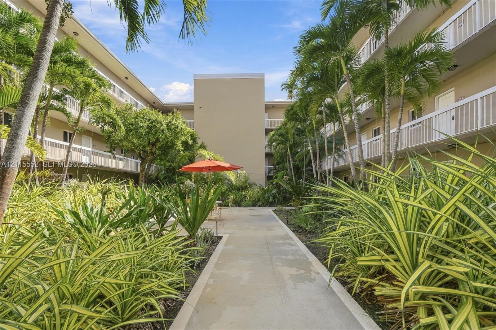 Central courtyard featuring concrete walkways, mature palm trees, tiered exterior balconies with white railings, and native tropical landscaping