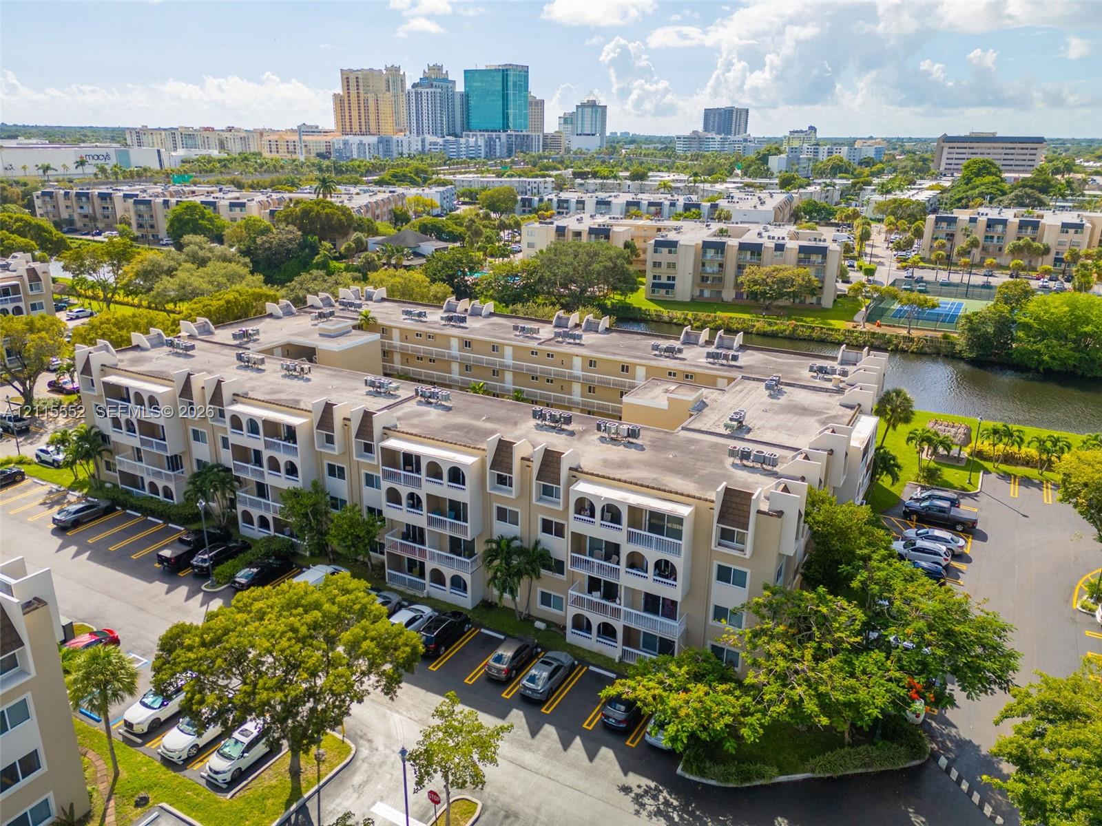 Multi-story residential complex featuring arched architectural detailing, private balconies, on-site surface parking, and waterfront grounds