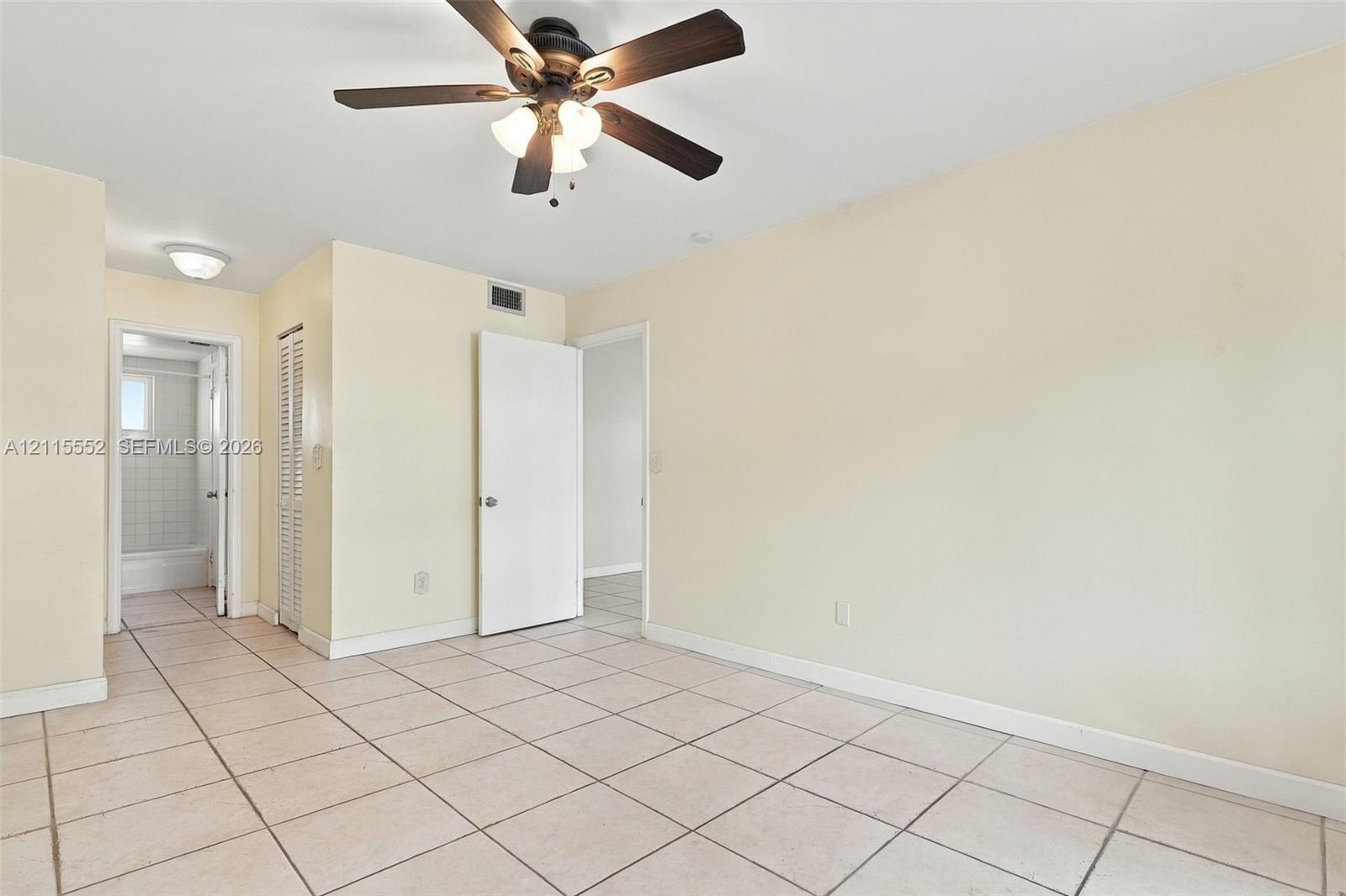 Neutral tile flooring, ceiling fan with integrated lighting, and louvered closet doors