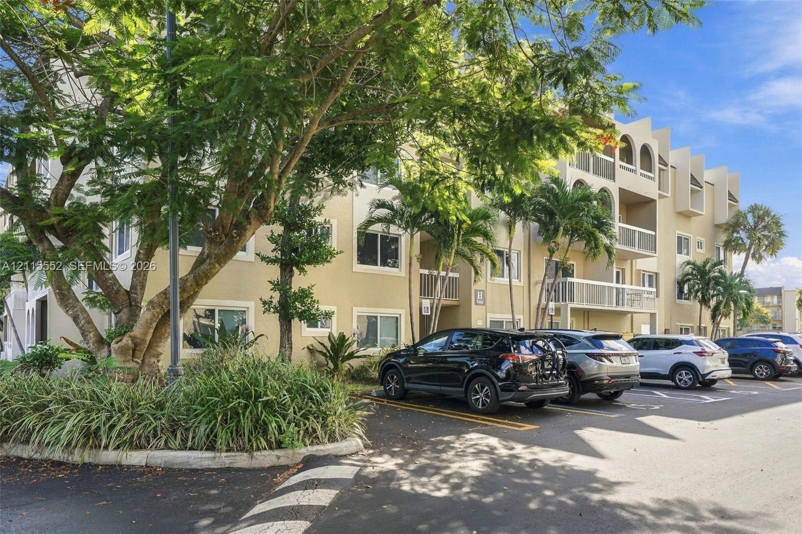 Multi-story building exterior featuring stucco siding, arched architectural detailing, private railed balconies, and surface parking