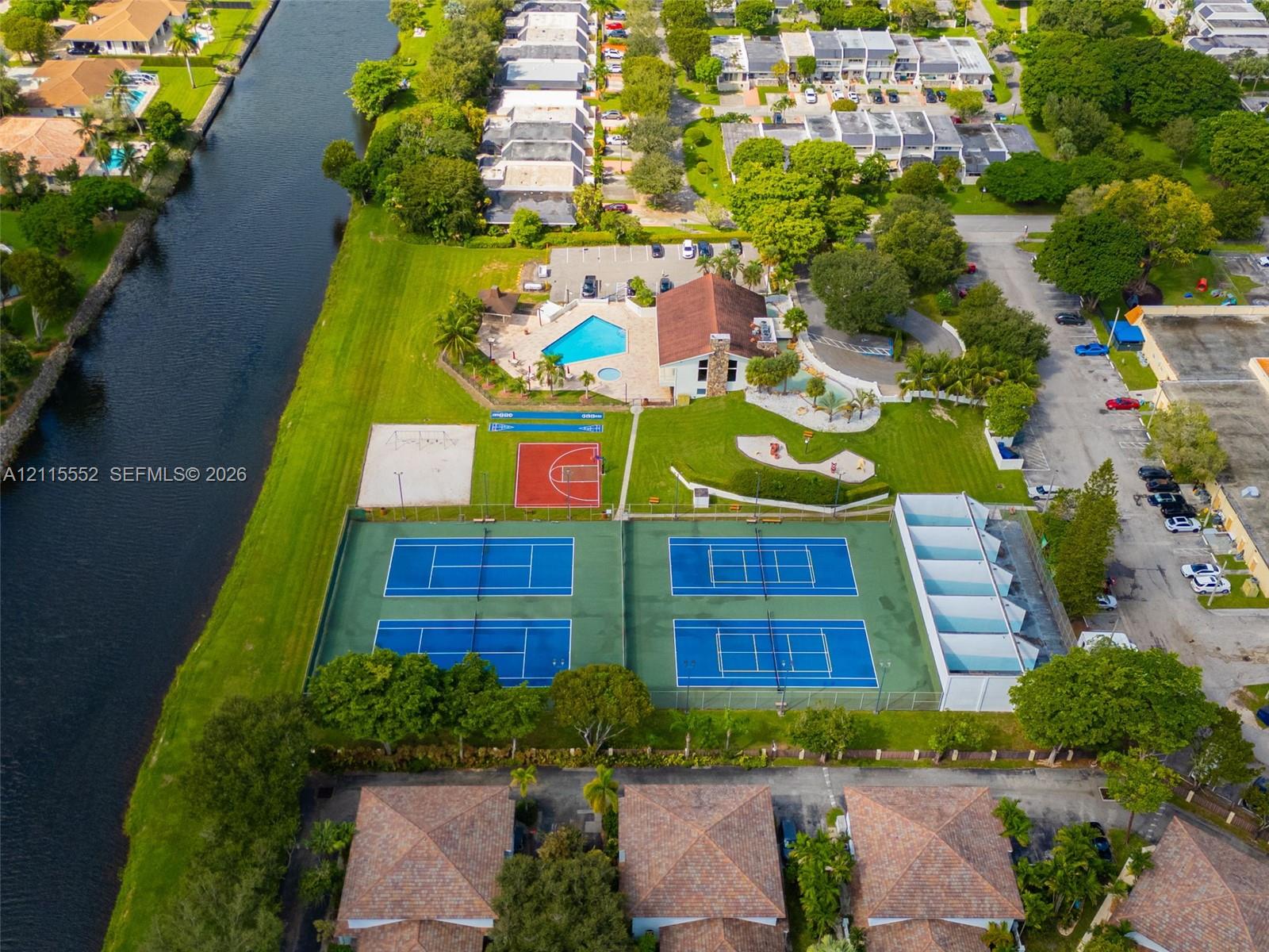Aerial perspective featuring waterfront grounds, four tennis courts, an outdoor swimming pool, a basketball court, and a sand volleyball court