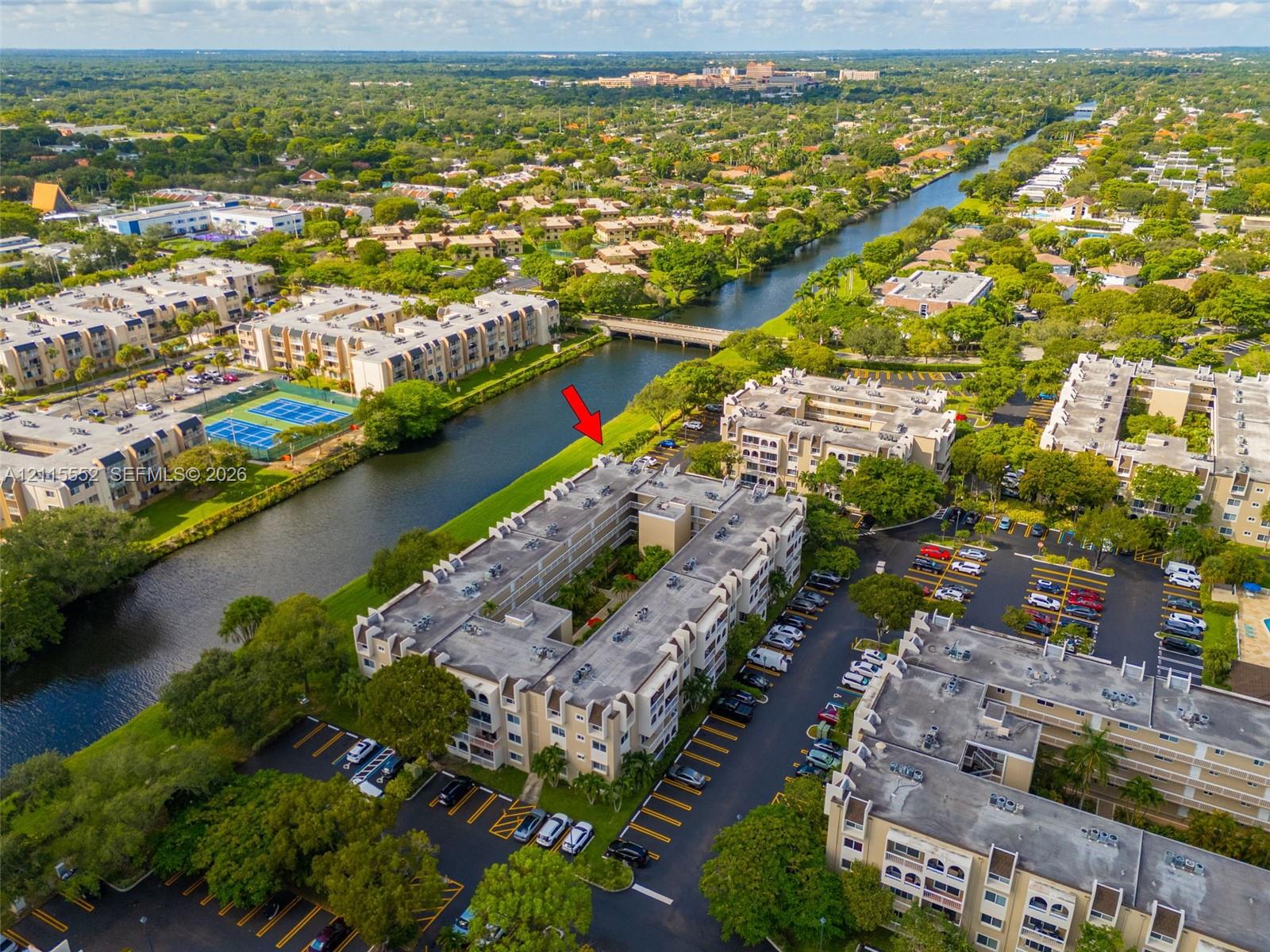 Aerial perspective of multi-story residential building featuring water frontage, dedicated surface parking, and exterior landscaping
