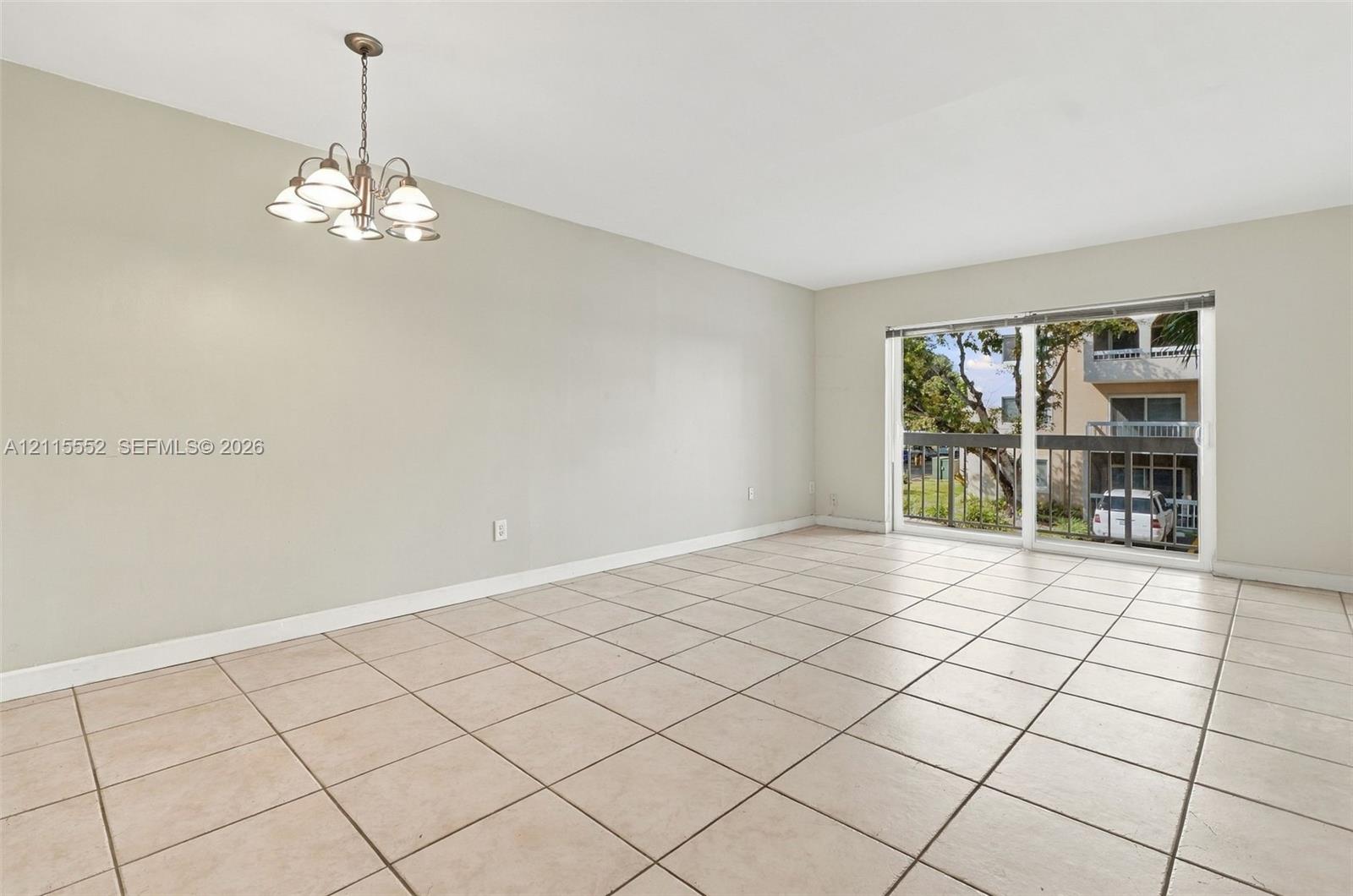 Neutral-tone interior space featuring ceramic tile flooring, a multi-light chandelier, and large sliding glass doors providing access to a private balcony with metal railing