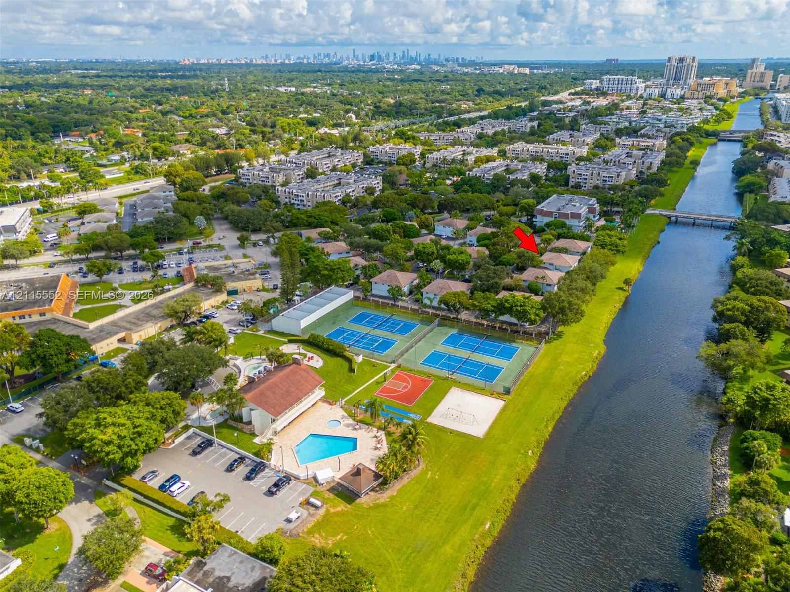 Aerial perspective of communal amenities featuring two tennis courts, a basketball court, a swimming pool, and a canal-side walking path