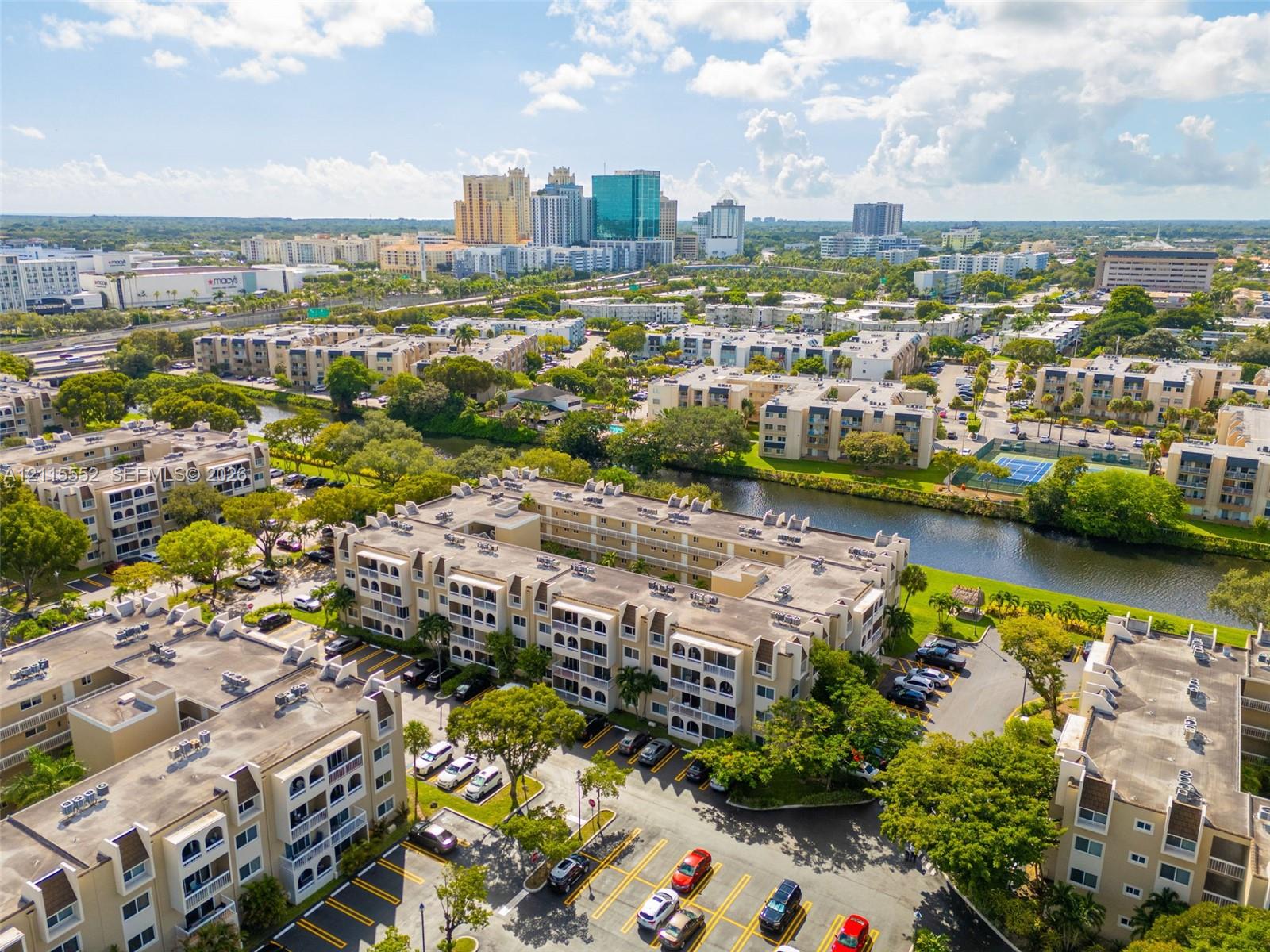 Multi-story residential complex featuring beige stucco facades, arched architectural detailing, balconies, and on-site surface parking